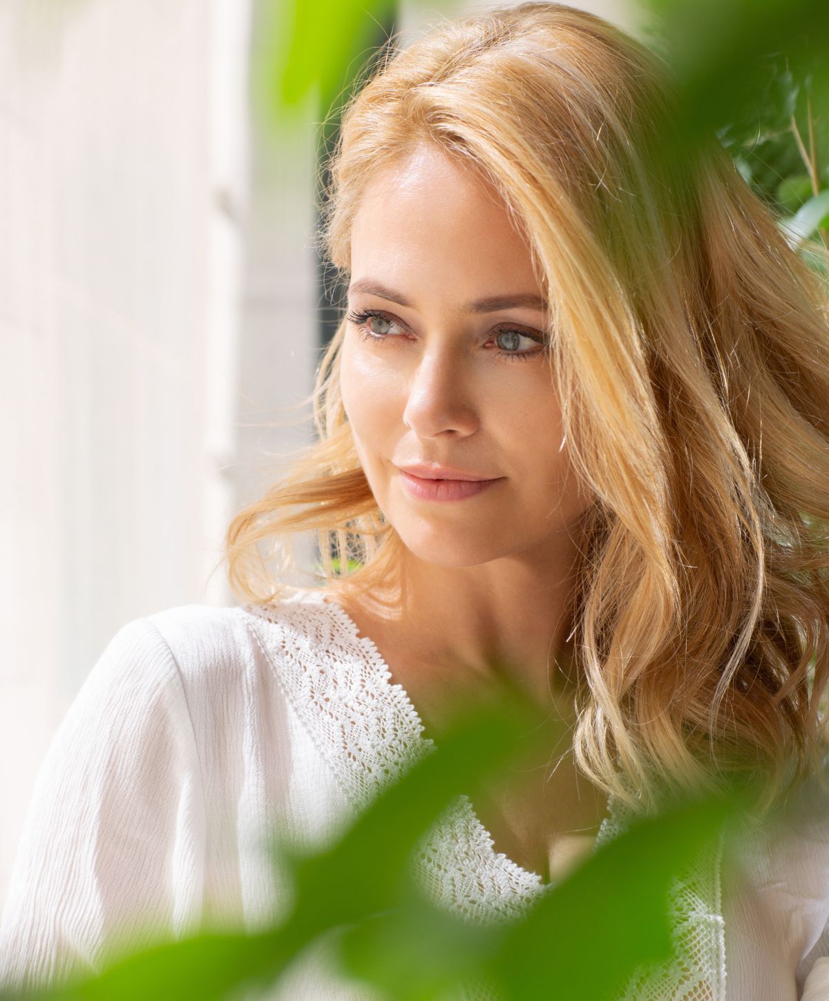 Woman with blonde hair surrounded by greenery.