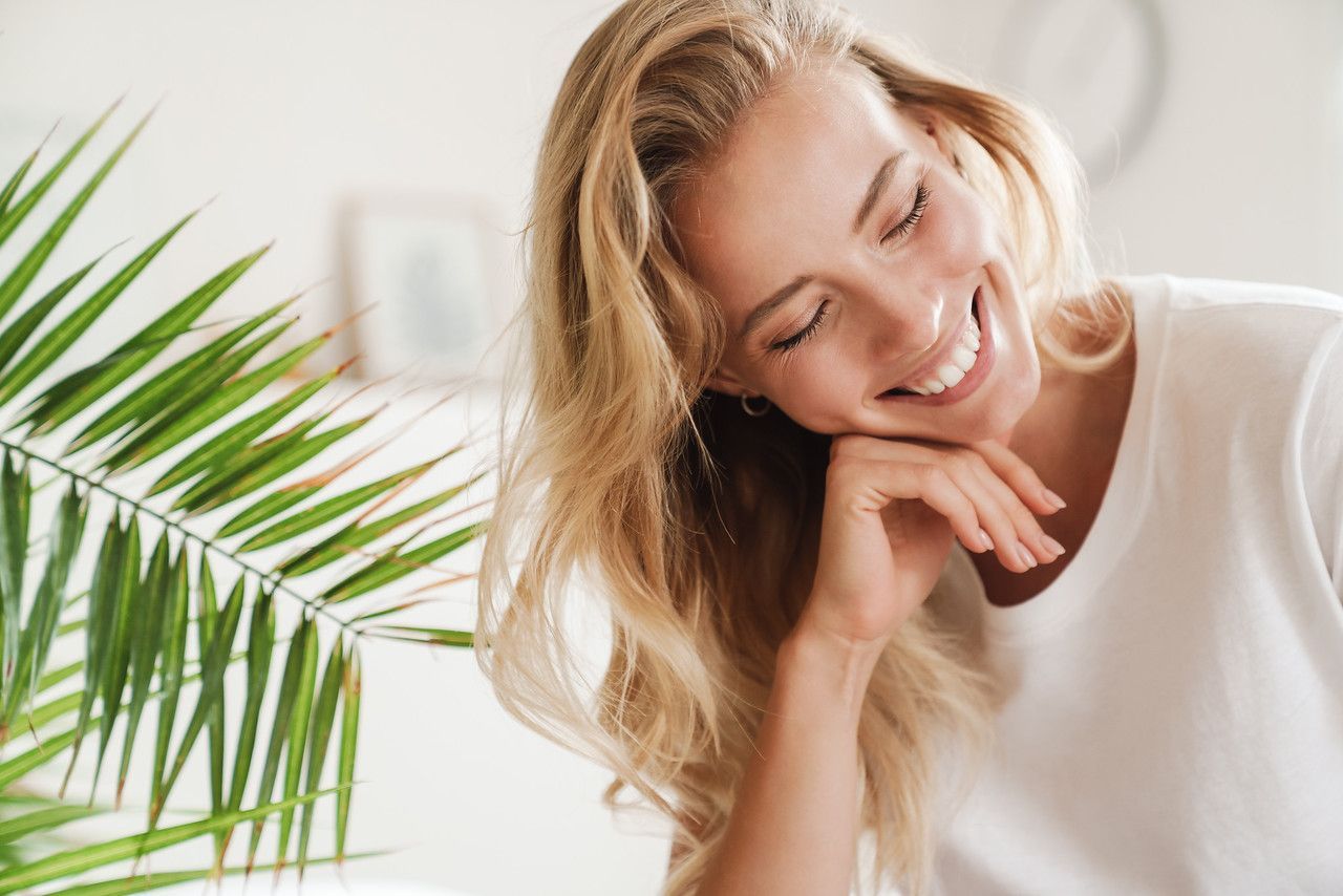 Smiling woman with blonde hair and greenery.