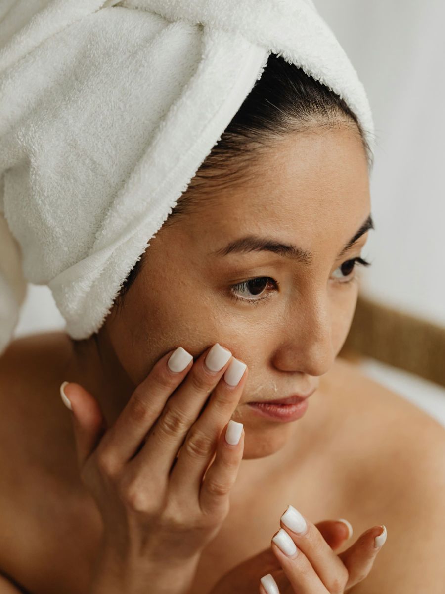 Woman applying skincare with towel on head.