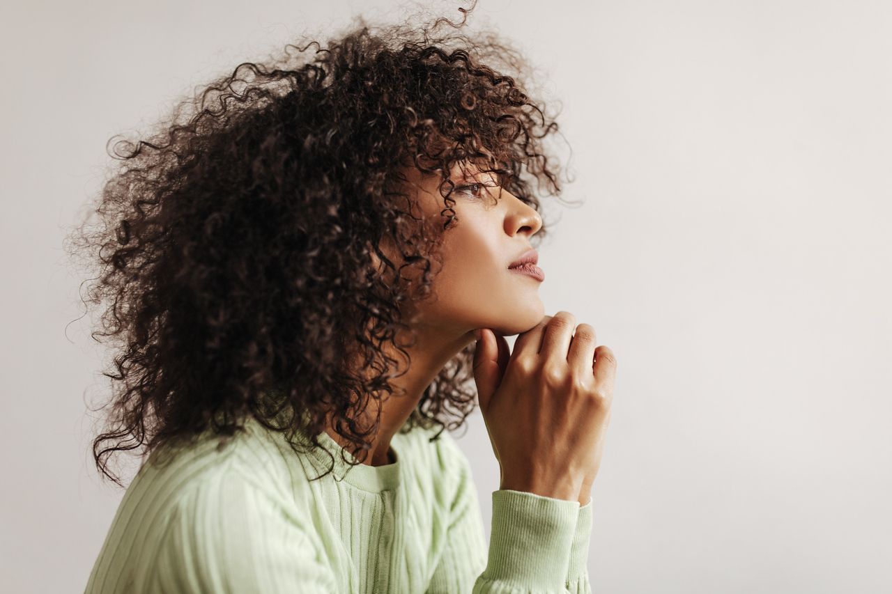 Woman with curly hair, pondering thoughtfully.